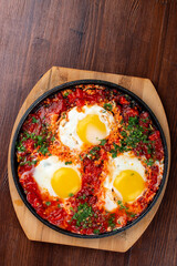Scrambled eggs at home with tomatoes in a frying pan. On a wooden background. Breakfast
