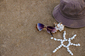 Fototapeta na wymiar Brown panama hat, sunglasses, seashell and sun made of small white pebbles lie on sand beach ocean shore. Atmosphere summer beach holiday, beach accessories, copy space, concept summertime.