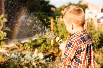 The boy enjoys a rainbow while watering in the garden