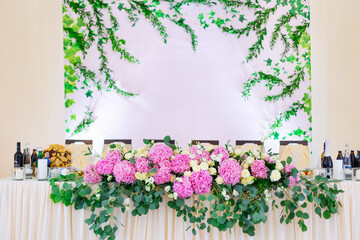 Lush floral arrangement on wedding table. Wedding presidium in restaurant. Banquet table for newlyweds with flowers. Luxury wedding decorations
