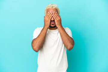 Young Colombian handsome man isolated on blue background covering eyes by hands