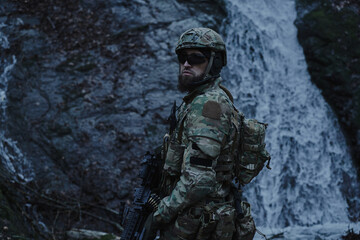 Portrait of airsoft player in professional equipment with machine gun in the forest. Soldier with...