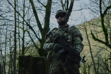 Obraz premium Portrait of airsoft player in professional equipment with machine gun in the forest. Soldier with weapons at war