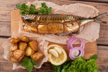 Composition smoked mackerel fish with garnish potatoes lemon greens onions served on wooden board plate top view