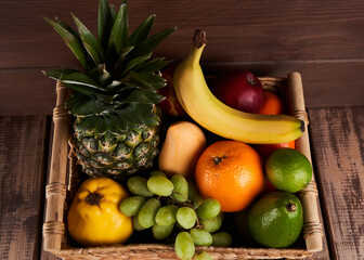 Mix of fresh juicy colorful exotic tropical fruits in basket on wooden background top view