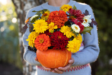 Woman in sweater holds pumpkin with bright bouquet in yard