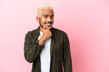 Young Colombian handsome man isolated on pink background looking to the side and smiling