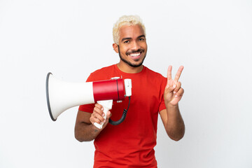Young Colombian handsome man isolated on white background holding a megaphone and smiling and...