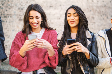 Two women best friends using smartphone together standing outdoors. Gen z young people using social...