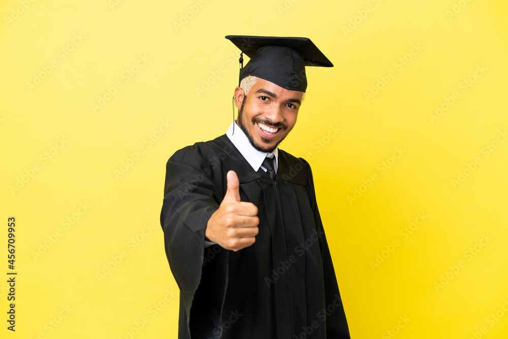 Wall mural Young university graduate Colombian man isolated on yellow background with thumbs up because something good has happened