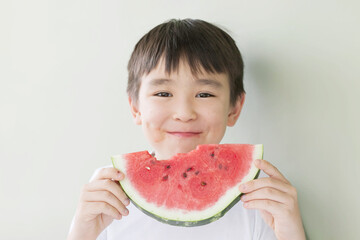 Happy cute asian child boy eating red watermealon indoors
