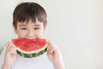 Happy cute asian child boy eating red watermealon indoors