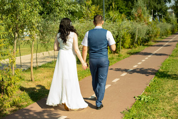 The newlyweds walk along the park path holding hands.