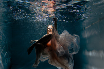 A girl with long dark hair swims underwater in a pink dress and with a crown on her head, like an underwater queen. Fairy tale suitable for advertising	