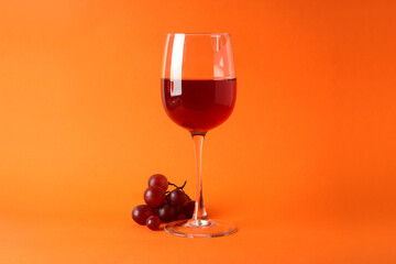 Glasses of red wine and grape on orange background