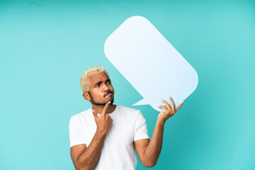 Young Colombian handsome man isolated on blue background holding an empty speech bubble and thinking