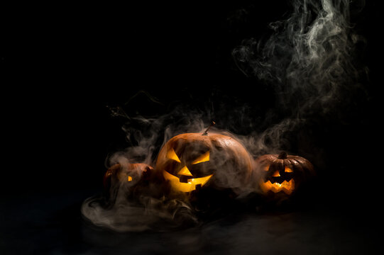 Pumpkins with carved grimaces and candles inside in the dark for halloween. Jack o latern in smoke.