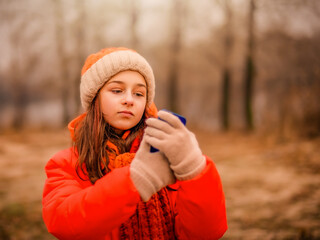Teenage girl looks into a smartphone in autumn or winter in the park. The girl is recording a video