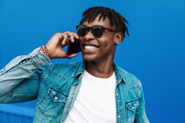 african man in sunglasses typing sms over blue background, 5g internet concept, high speed internet on phone