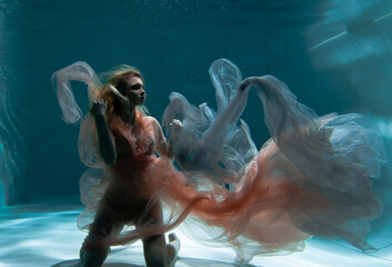 A girl with long dark hair swims underwater in a pink dress and with a crown on her head, like an underwater queen. Fairy tale suitable for advertising	