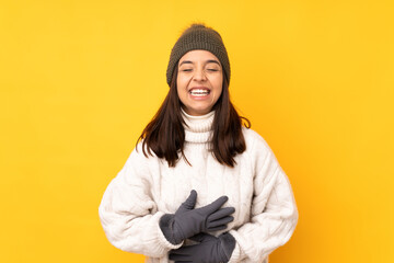 Young woman with winter hat over isolated yellow background smiling a lot