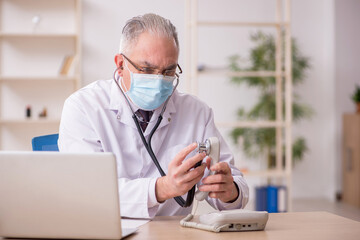 Old male doctor working in the clinic during pandemic