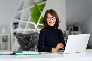 Attractive businesswoman wearing turtleneck sweater while working on laptop at the office