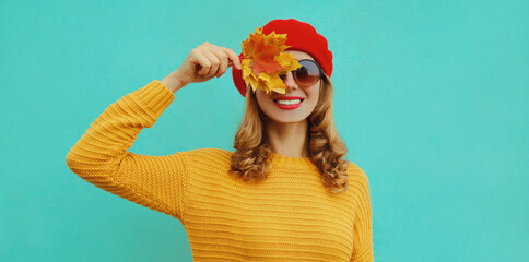 Autumn portrait of happy smiling young woman with yellow maple leaves wearing a knitted sweater,...