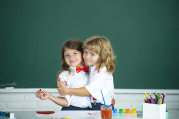 School friends hugging. Two school kids, girl and boy holding hands going at school class in classroom. Two primary school children in a classroom hugging each other.