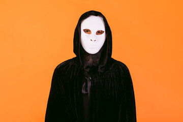 Portrait of a person in white killer Halloween mask, cape and hood looking at camera, dressed for...
