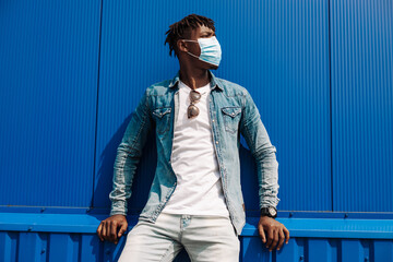 portrait of an afro american black man wearing a protective mask from the coronavirus, on a blue background