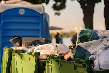 Overflowing waste bins and portable toilet after public event, container for temporarily storing...