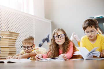 Four cute children in glasses lying on the floor indoors with books