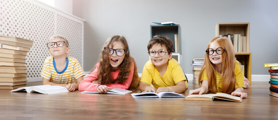 Four cute children in glasses lying on the floor indoors with books