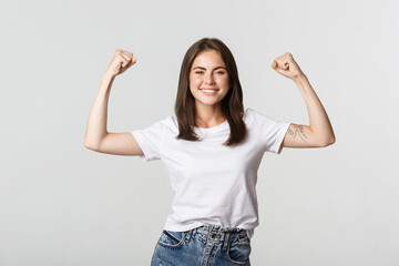 Portrait of confident attractive girl flex biceps to show strengths, smiling sassy