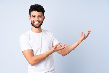 Young Moroccan man isolated on blue background extending hands to the side for inviting to come