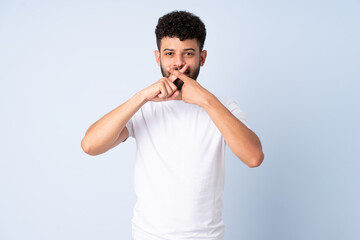 Young Moroccan man isolated on blue background showing a sign of silence gesture