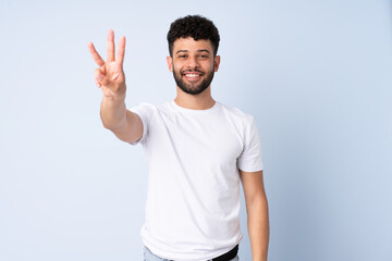 Fototapeta premium Young Moroccan man isolated on blue background happy and counting three with fingers