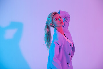 Creative portrait of a beautiful stylish girl in a fashion elegant blue jacket on a colored neon...