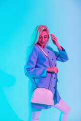 Happy beautiful young girl with blonde hair in elegant fashion with a blue blazer and a trendy white handbag in studio with a pastel colored
