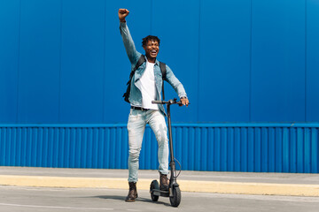 young african american man on an electric scooter, rides on road, in city against the background of...