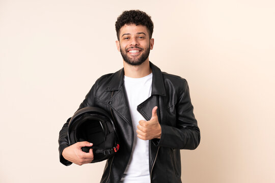 Young Moroccan man with a motorcycle helmet isolated on beige background giving a thumbs up gesture
