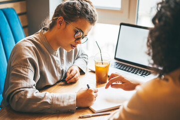 Young caucasian woman and man working and studying at cafe with laptop, discussing tasks and preparing for exam. Online education and Internet courses