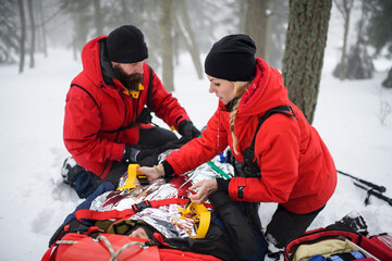Mountain rescue service provide operation outdoors in winter in forest, injured person in stretcher.