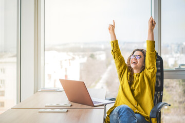Happy successful businesswoman in yellow shirt raising fists with ambition. Women going up career ladder. Business achievement and promotion concept - obrazy, fototapety, plakaty