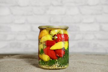 Mini chili peppers of red, yellow and orange colors, canned in glass jars with herbs, on a wooden table. Homemade pickled peppers in Asian style. Preparations for the winter. Copy space