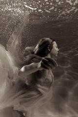 A girl with long hair swims underwater in a pink dress. She looks like an underwater dragon....
