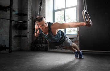 Fototapeta na wymiar fitness, sport, bodybuilding and people concept - young man exercising on gymnastic rings in gym
