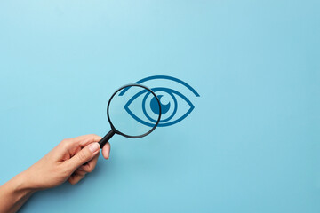 A person examines the eye through a magnifying glass. Symbol for the diagnosis of eye diseases - obrazy, fototapety, plakaty