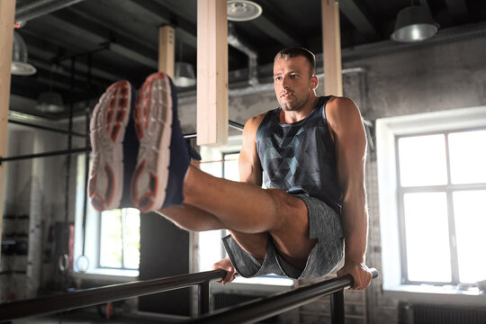 fitness, sport, bodybuilding and people concept - young man doing abdominal exercise on parallel bars in gym